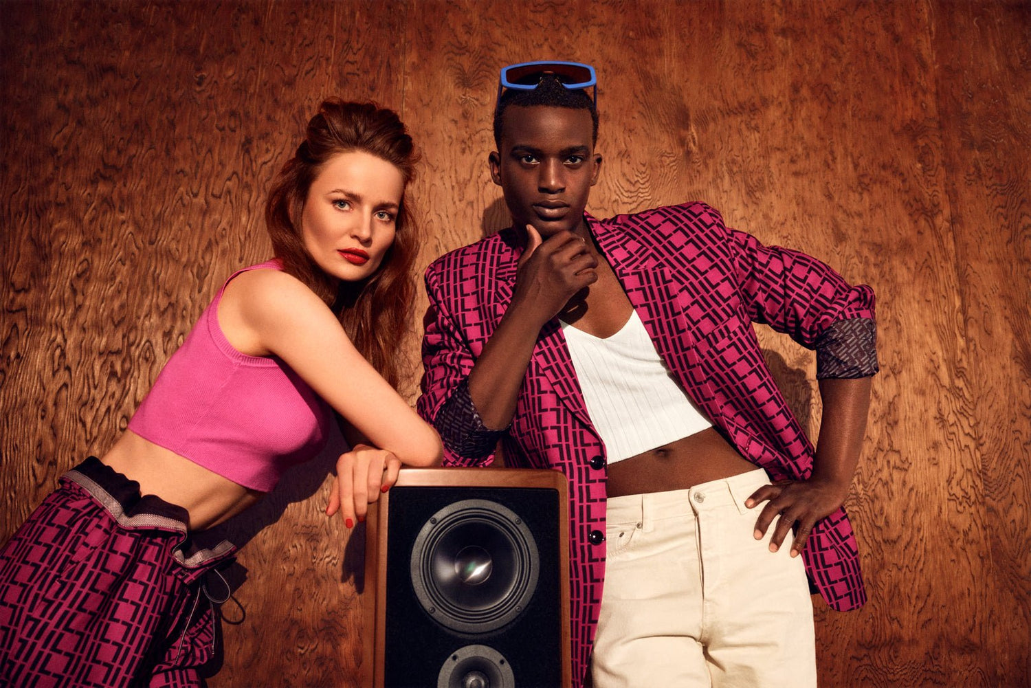 Suit NO.1 -ILLEGAL LUXURY- Black Male Model and white female Model standing at a speaker . Magenta suit with Black IL Pattern